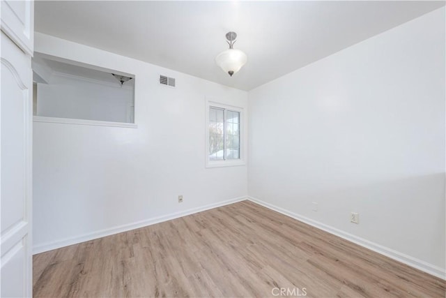 spare room with light wood-type flooring, visible vents, and baseboards