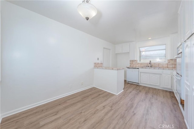 kitchen with white appliances, white cabinetry, light countertops, light wood-type flooring, and backsplash