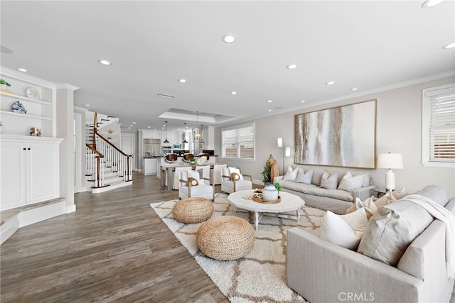 living room with dark wood finished floors, stairway, ornamental molding, a tray ceiling, and recessed lighting