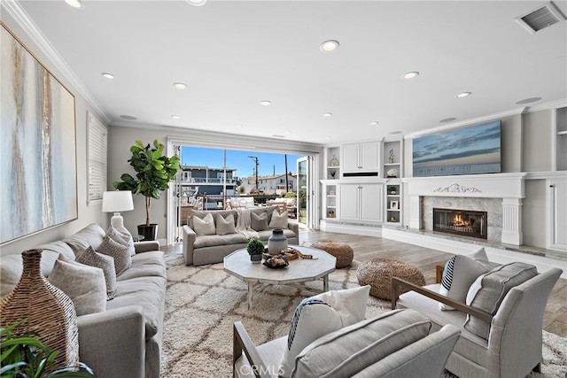 living room with visible vents, built in features, a premium fireplace, ornamental molding, and recessed lighting