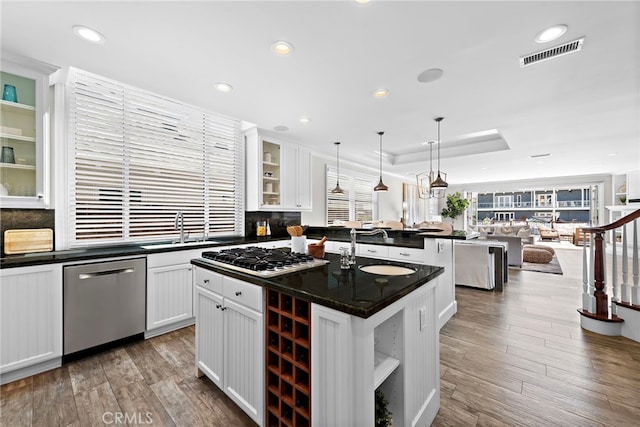 kitchen featuring decorative light fixtures, glass insert cabinets, appliances with stainless steel finishes, open floor plan, and an island with sink