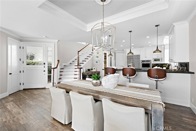 dining room featuring a tray ceiling, crown molding, dark wood finished floors, an inviting chandelier, and stairs