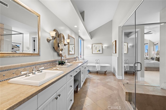 ensuite bathroom with lofted ceiling, a soaking tub, visible vents, wainscoting, and a sink