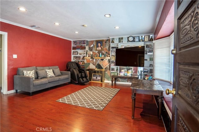 living room featuring built in features, hardwood / wood-style flooring, crown molding, and a stone fireplace