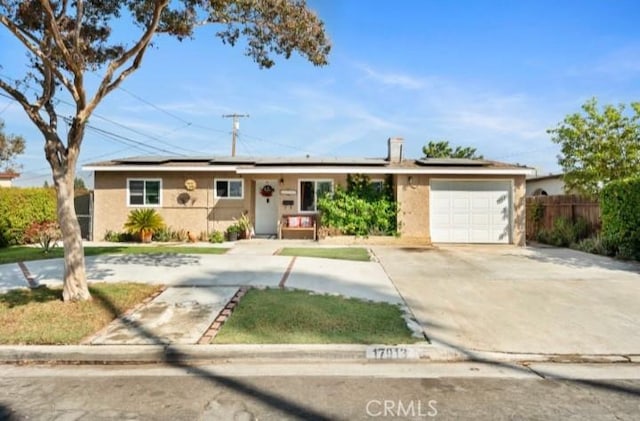 single story home featuring a garage, roof mounted solar panels, fence, and driveway