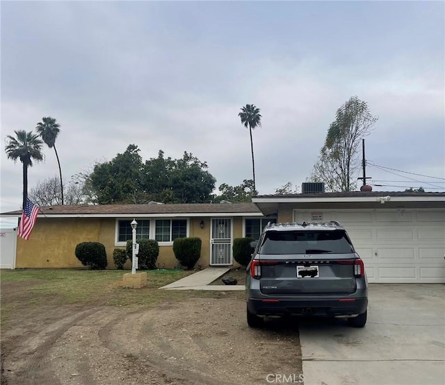 ranch-style house featuring a garage, stucco siding, driveway, and central air condition unit