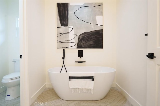 bathroom featuring a soaking tub, toilet, and baseboards