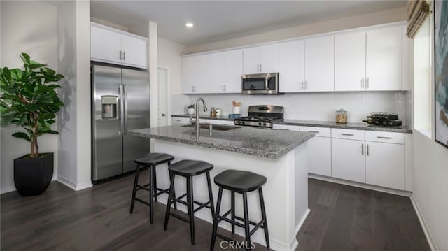 kitchen featuring stainless steel appliances, an island with sink, white cabinets, decorative backsplash, and sink