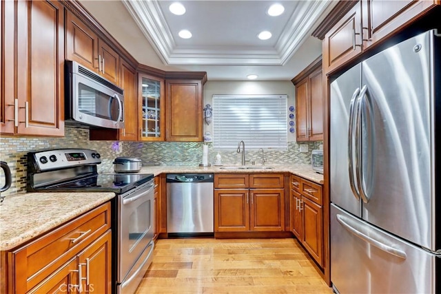 kitchen with appliances with stainless steel finishes, sink, light hardwood / wood-style flooring, a tray ceiling, and ornamental molding