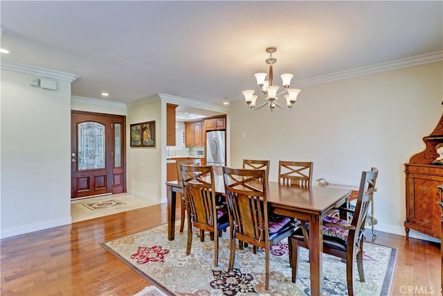 dining space featuring light wood-type flooring, ornamental molding, and a chandelier