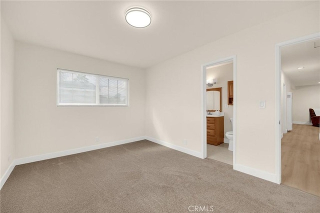 unfurnished bedroom featuring carpet floors, ensuite bathroom, and baseboards