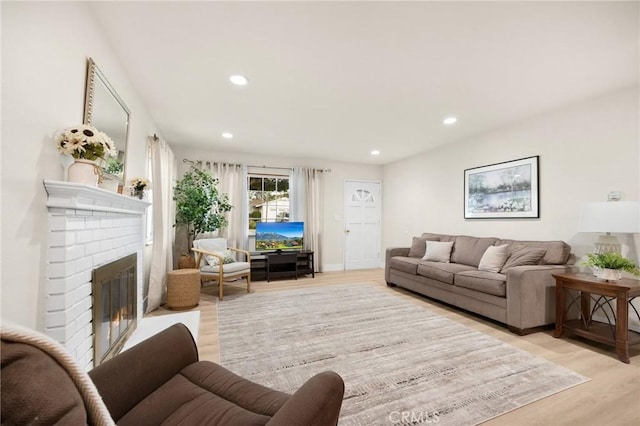 living area with light wood-style flooring, a brick fireplace, and recessed lighting