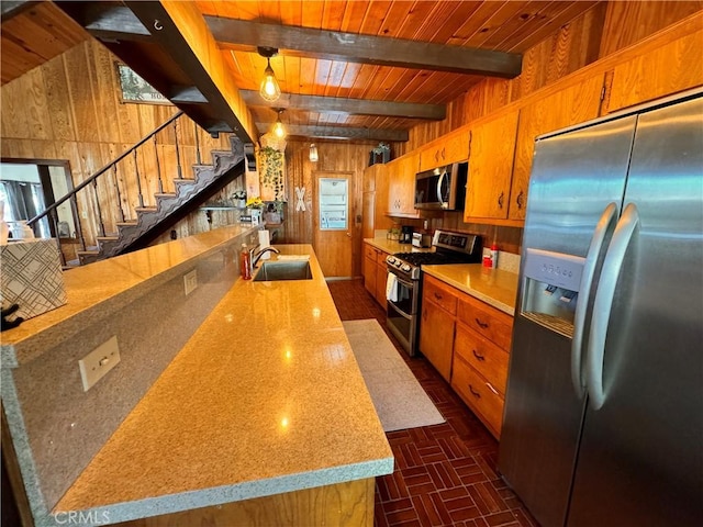 kitchen with beam ceiling, brown cabinets, stainless steel appliances, a sink, and wooden walls