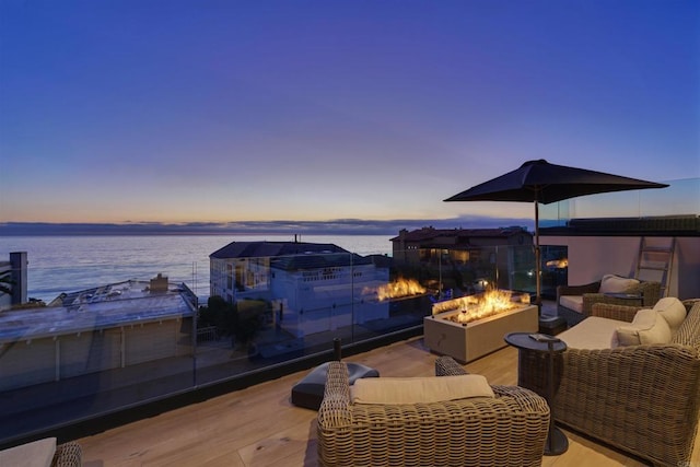 deck at dusk featuring a water view and an outdoor living space with a fire pit