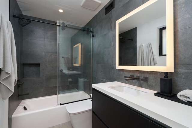 full bathroom featuring toilet, tile walls, shower / bath combination with glass door, and vanity