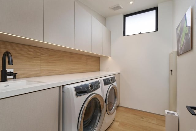 laundry area with cabinets, washing machine and dryer, sink, and light hardwood / wood-style flooring