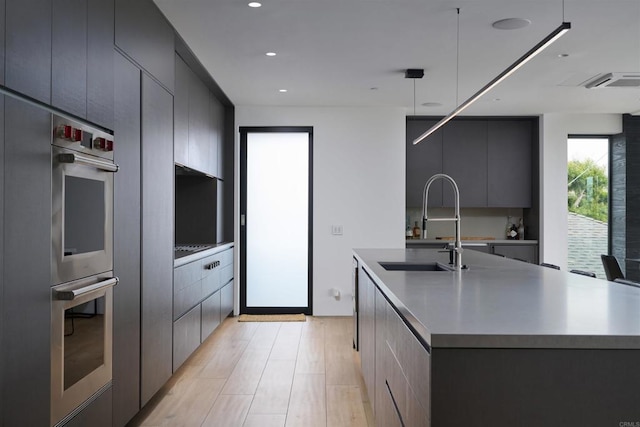 kitchen with sink, light hardwood / wood-style flooring, a kitchen island with sink, and decorative light fixtures