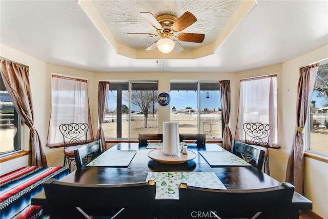 dining area with a tray ceiling, ceiling fan, and a textured ceiling