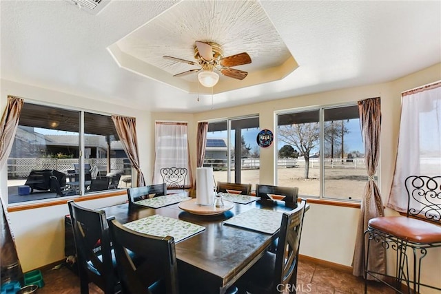 dining space with a tray ceiling, a healthy amount of sunlight, ceiling fan, and baseboards