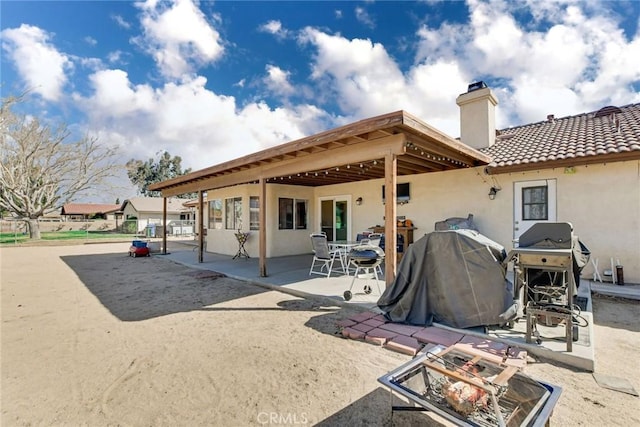 rear view of house with a tiled roof, a chimney, a patio area, and stucco siding