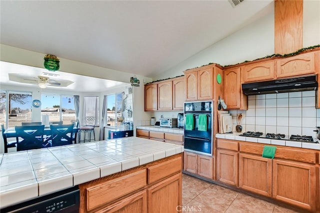 kitchen with tile counters, dishwasher, under cabinet range hood, gas stovetop, and a warming drawer