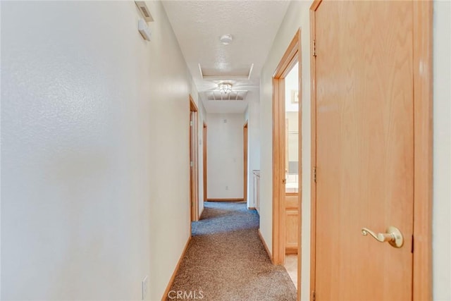 corridor featuring light colored carpet, a textured ceiling, and baseboards