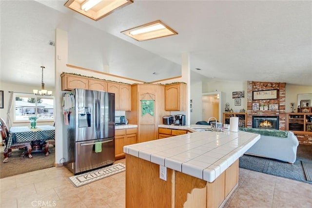 kitchen featuring a peninsula, a sink, vaulted ceiling, open floor plan, and stainless steel refrigerator with ice dispenser