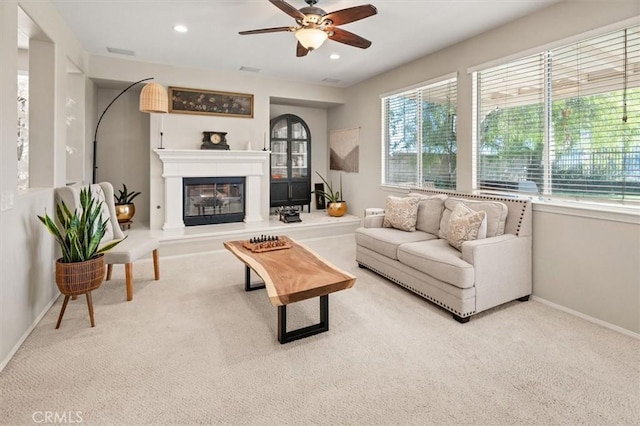 carpeted living area featuring baseboards, a glass covered fireplace, visible vents, and recessed lighting