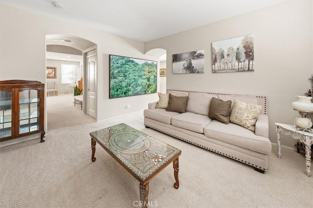 living area featuring arched walkways, baseboards, and light colored carpet