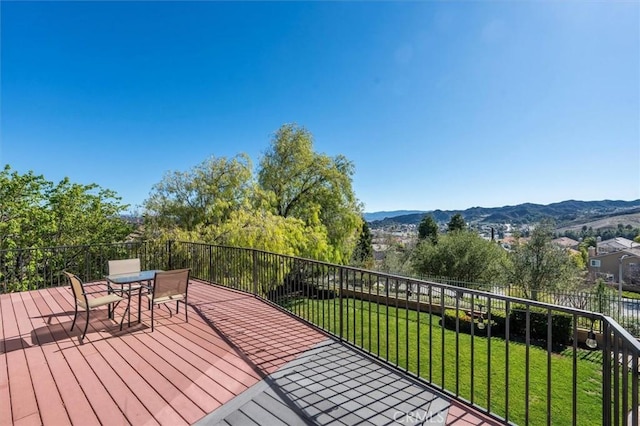 deck with outdoor dining space, a mountain view, and a yard