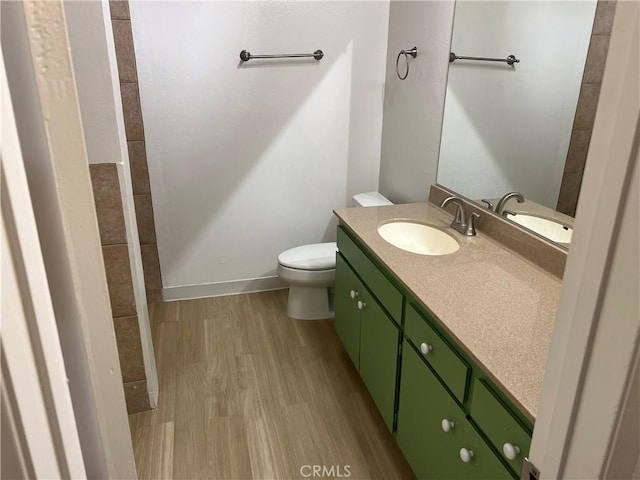 bathroom featuring baseboards, wood finished floors, toilet, and vanity