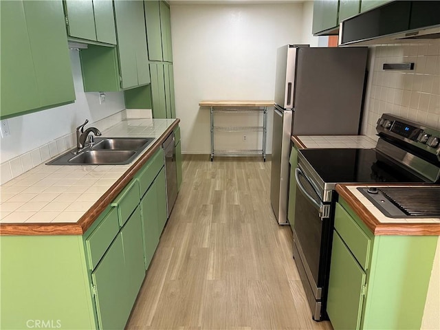 kitchen with light wood finished floors, a sink, under cabinet range hood, green cabinets, and appliances with stainless steel finishes