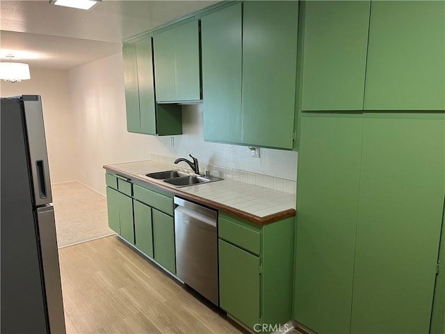 kitchen featuring a sink, tile counters, stainless steel appliances, green cabinets, and light wood-type flooring
