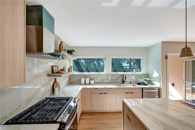 kitchen with stainless steel appliances, hanging light fixtures, light brown cabinetry, a sink, and wall chimney range hood