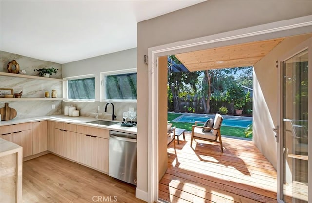 kitchen featuring plenty of natural light, light countertops, light wood-type flooring, stainless steel dishwasher, and a sink