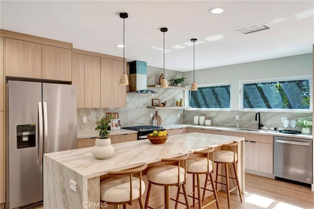 kitchen featuring a center island, visible vents, appliances with stainless steel finishes, a sink, and wall chimney range hood