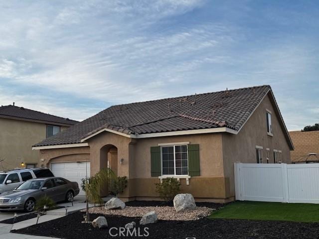 view of front of home featuring a garage, driveway, a tile roof, fence, and stucco siding