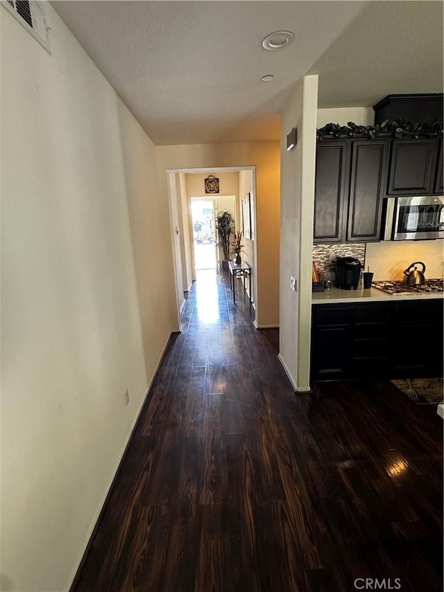 hallway with dark wood-style floors, baseboards, and visible vents