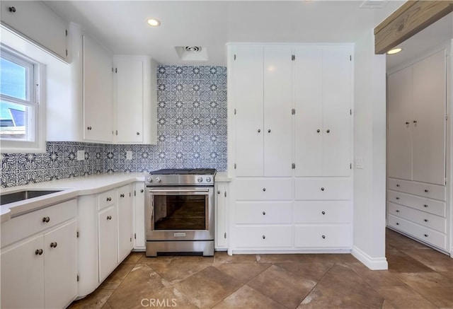 kitchen featuring stainless steel gas stove, sink, white cabinetry, and decorative backsplash