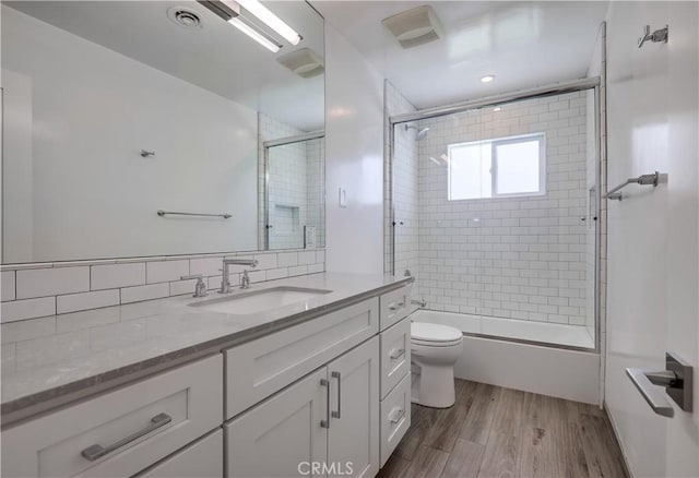 full bathroom featuring hardwood / wood-style floors, vanity, toilet, enclosed tub / shower combo, and tasteful backsplash