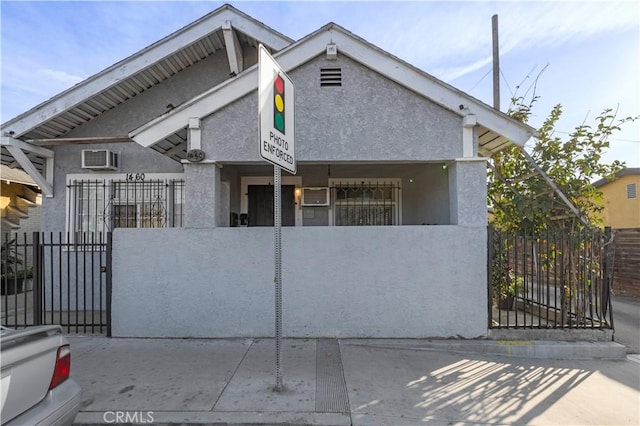 view of front of house with a fenced front yard, a wall mounted air conditioner, a gate, and stucco siding