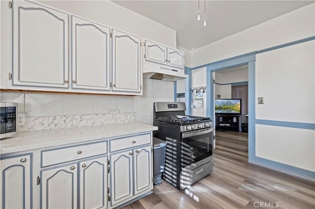kitchen featuring stainless steel gas stove, tasteful backsplash, white cabinets, light wood-style flooring, and under cabinet range hood