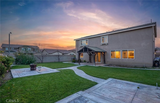 back house at dusk featuring a patio and a lawn