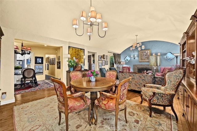 dining room featuring wood finished floors, a fireplace, vaulted ceiling, and an inviting chandelier