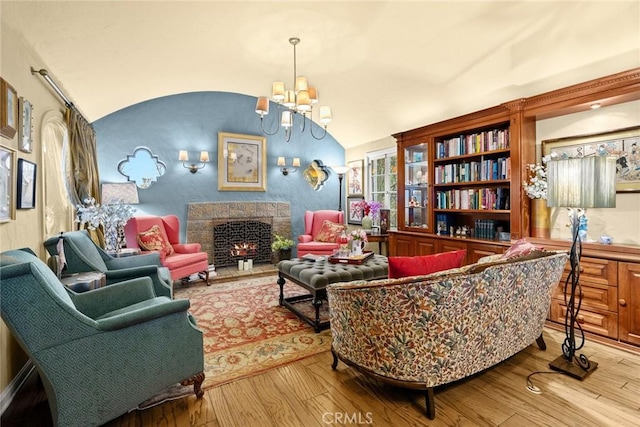 sitting room featuring a chandelier, light wood-type flooring, vaulted ceiling, and a lit fireplace