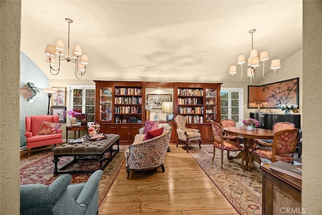 living area featuring vaulted ceiling, a textured wall, light wood-style floors, and an inviting chandelier