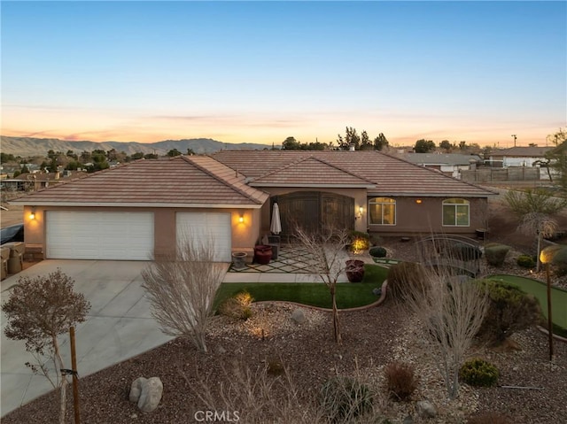 view of front of house featuring a tile roof, stucco siding, concrete driveway, a mountain view, and a garage