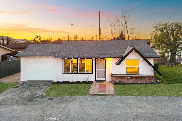 view of front of house with brick siding, aphalt driveway, roof with shingles, an attached garage, and a front yard