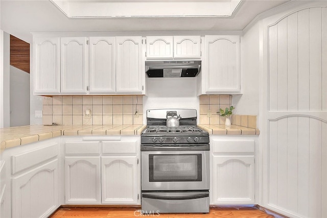 kitchen featuring white cabinetry, light wood-type flooring, exhaust hood, stainless steel gas range, and decorative backsplash