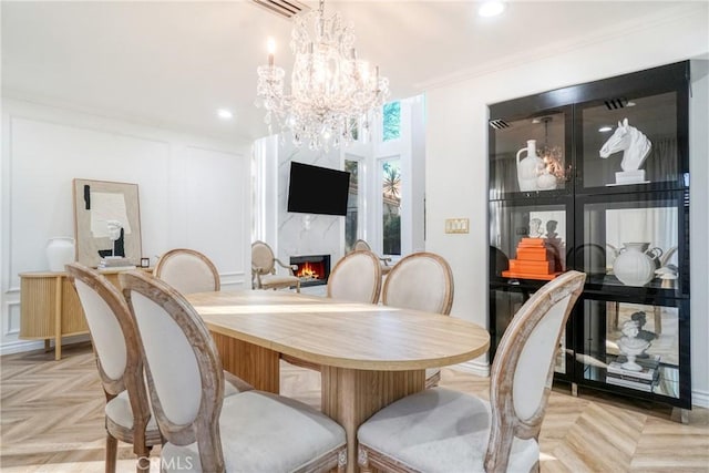 dining space featuring a chandelier, light parquet flooring, ornamental molding, and a fireplace